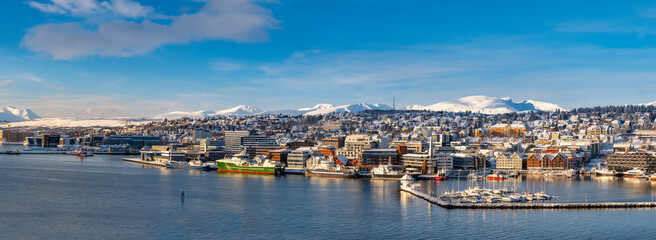 Obraz premium Panoramic view to Tromso harbor. White yacht sailing in the port of Tromso at sunset. Frost and first snow. Colorful winter clouds. Northern Norway