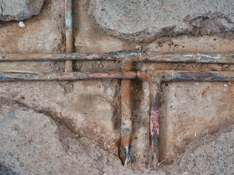 Exposed, leaking copper central heating pipes, badly corroded after being buried in the concrete floor slab of a house of around 60 years.