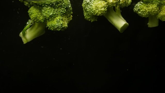 Background video of broccoli falling into water for cooking. The green vegetable is filled with useful and important substances for the body. High quality 4k footage