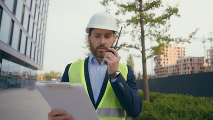 Caucasian professional contractor foreman worker talking in walkie talkie middle-aged builder in hard hat talk remote radio man architect engineer repairman work in construction sites check blueprint