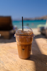 Closeup view of an iced greek coffee, also known as cafe frappe with a straw at a beach in Ios Greece