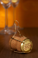 Champagne cork, Happy new year and 2024 text on golden cap. Two glasses on wooden background.