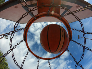 Santo Tirso, Portugal, January 1, 2022: An iron outdoor basketball hoop with blue sky background in the sports field. The basketball hoop or ring. Basketball going through the basket.