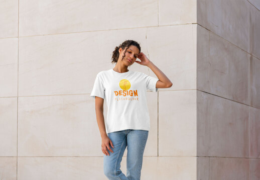 Mockup of woman sitting wearing customizable t-shirt by corner of building