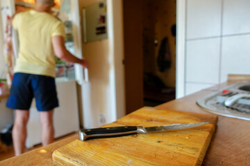Knife on a wooden cutting board. In the background is a silhouette of a man near the refrigerator.