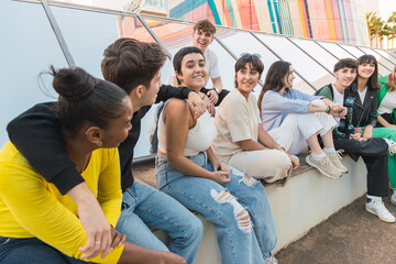 Group of diverse friends having fun and sitting on marble bench near glass walls