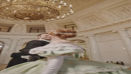 Vertical shot of beautiful Renaissance couple dancing under gold crystal chandelier in luxurious ballroom