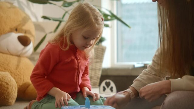 Cute child on the floor plays board game with her mom, using hammer and other figures. True kid's interest and emotions, been excited, having fun. Educational games concept. High quality 4k footage