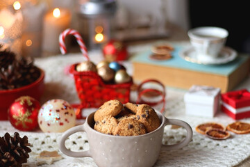Various colorful Christmas decorations, soft blanket, cup of tea, sweet snacks and lit candles on the table. Cozy Christmas atmosphere at home. Selective focus.