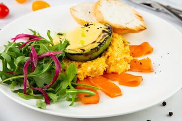 a mix of salmon, arugula salad, white bread and baked avocado with cheese side view