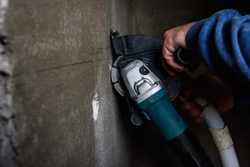 Fotobehang Worker holding angle grinder with two diamond discs for cutting grooves in wall. © Natallia