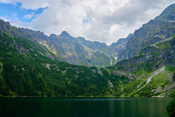 Fototapeta na wymiar Amazing view on mountains range near beautiful lake at summer day. Tatra National Park in Poland. Panoramic view on Morskie Oko or Sea Eye lake in Five lakes valley