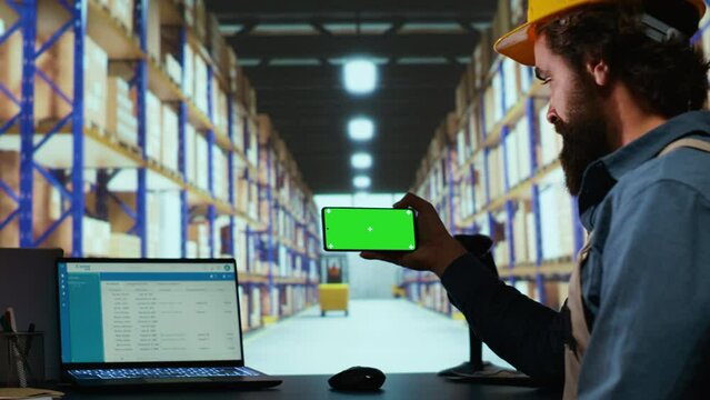 Storehouse advisor checks greenscreen on phone layout, working on package transport and logistics in industrial warehouse. Quality control manager uses isolated copyspace display.