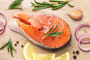 One raw trout steak with rosemary, lemon, onion, pepper and garlic on baking paper, top view