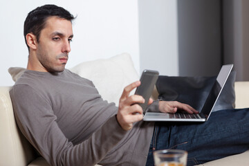 Young man working from home using laptop and smart phone