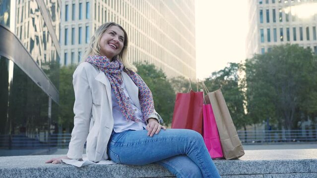 Smiling blonde woman in commercial zone with shopping paper bags after shopping.
