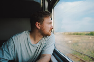 A man with a beard and mustache in a blue t-shirt while traveling by Railway train, sitting in the...