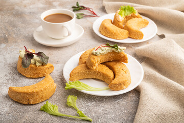 Homemade salted crescent-shaped cheese cookies, cup of coffee on brown concrete. side view