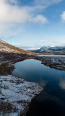Aerial photo of a calm Norwegian mountain alpine lake in the Winter in the Arctic Circle of Norway.  Cloudy skies with snowcapped mountains.  Shot on a drone