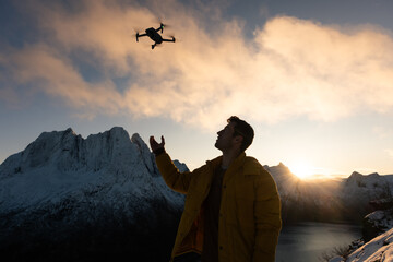 A man in a yellow jacket catching a drone during takeoff on a snowcapped mountain in the Arctic...