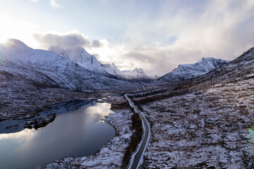 Aerial photo of a calm Norwegian mountain alpine lake in the Winter in the Arctic Circle of Norway.  Cloudy skies with snowcapped mountains.  Shot on a drone