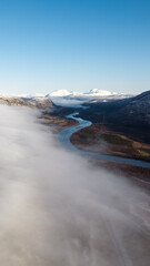 Beautiful aerial of river in Northern Norway covered with clouds and fog surrounded by mountains.  Winding river shot on a drone.
