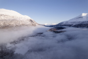 Beautiful aerial of river in Northern Norway covered with clouds and fog surrounded by mountains.  Winding river shot on a drone.