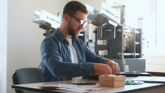 Raw material, bunch of cardboards. Handsome man is working at the factory of creating eco boxes.