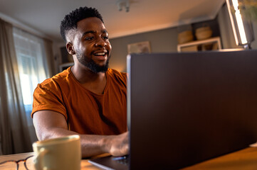 Young African American man sitting at home using laptop for video call.