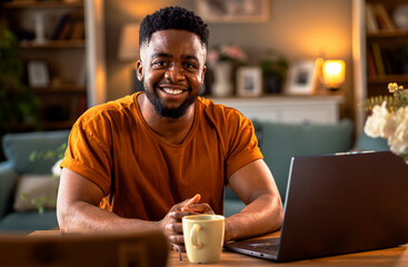 Portrait of young African American man sitting at home using laptop for video call.