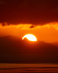 Telephoto image of large setting sun overtop a fjord mountain in Norway.  Beautiful orange sun...