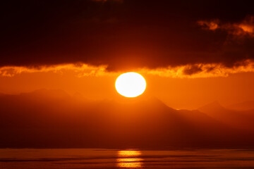 Telephoto image of large setting sun overtop a fjord mountain in Norway.  Beautiful orange sun...
