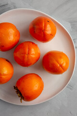 Organic Persimmon Fruit on a Plate on a gray background, top view. Flat lay, overhead, from above.