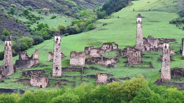View of the medieval Targim tower complex in the Caucasus mountains surrounded by greenery. The Caucasus Mountains on a cloudy day in Ingushetia. Russia, 4K.