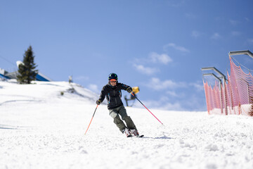 Professional skier skiing on slopes in a mountain winter resort. Sunny day with clear sky.