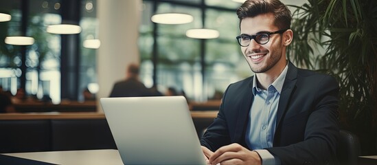 Businessman in office lobby working on laptop smiling copy space image