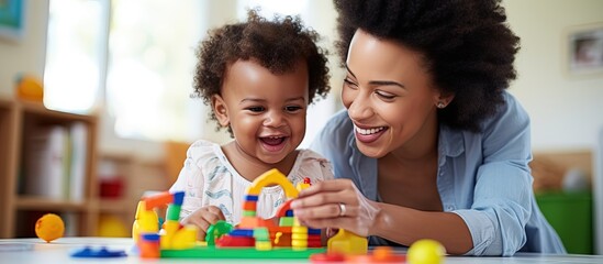 An African child plays with educational toys while supported by his mother and kindergarten teacher copy space image - obrazy, fototapety, plakaty