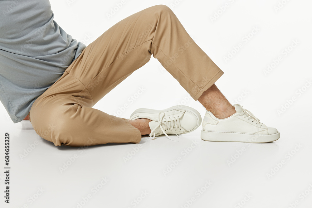 Wall mural man wearing white sneakers and beige pants sitting on floor