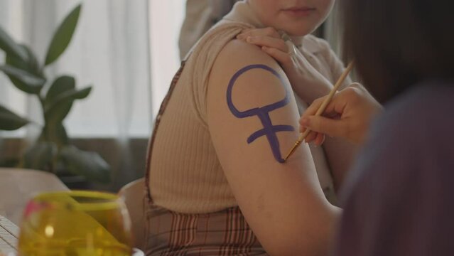 Cropped shot of unrecognizable female protesters drawing purple feminism symbol on shoulder before going on meeting