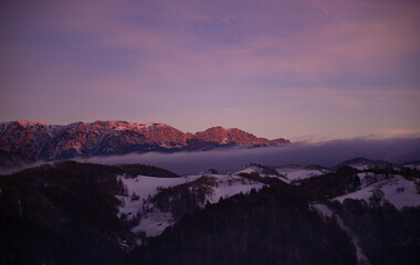 Fairy tale landscape with a rocky mountain full of snow at sunset. A village of traditional Romanian old houses spread over a valley.