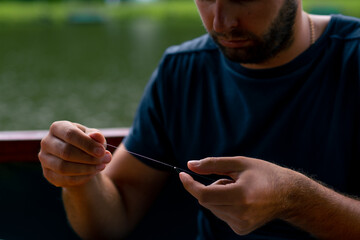 a young man strings a fishing line or a fly on a hook for fishing feeder free style method