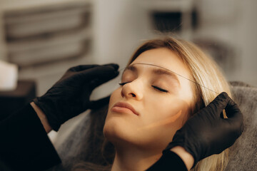 Marking of eyebrows. Permanent brow makeup. Markings with white paste and measuring ruler. Permanent make up artist in black gloves