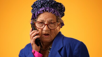 Closeup of funny crazy happy elderly old toothless woman talking on mobile cell phone wearing glasses isolated on solid yellow background studio portrait.  - obrazy, fototapety, plakaty