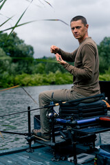 Portrait of a serious fisherman stringing a bait on the hook of a fishing rod for catching river...