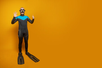 Scuba diver man showing six fingers up on yellow studio wall background - obrazy, fototapety, plakaty