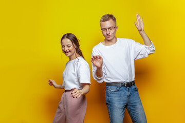 Happy laughing couple in casual wear dancing against yellow studio wall background