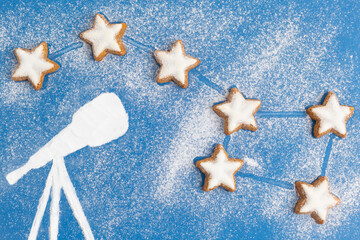 Big dipper made from cookies in form of stars and telescope made from sugar powder on blue sky...
