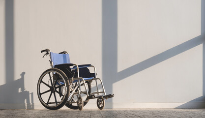 Empty wheelchair on tile floor with sunlight and shadow on gray interior wall surface