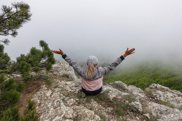 Obraz premium A picturesque mountain landscape in the clouds on Ai-Petri mountain in the Crimea. A woman on the background of a high-altitude landscape with trees in the clouds. Fog on the mountain.