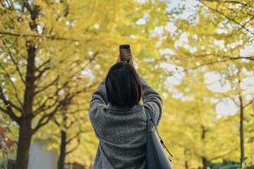 秋の紅葉をスマホで撮影する女性の後ろ姿